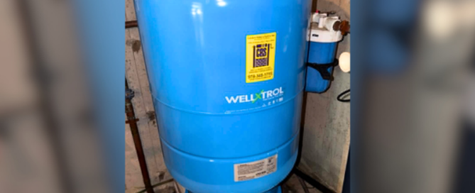 Blue Well-X-Trol pressure tank installed in a residential well water system, connected to plumbing and filtration components in a basement utility area.