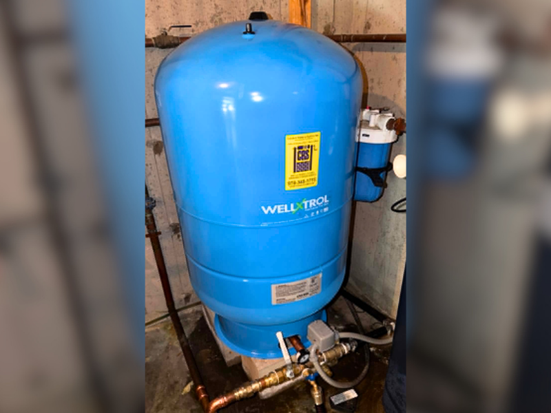 Blue Well-X-Trol pressure tank installed in a residential well water system, connected to plumbing and filtration components in a basement utility area.